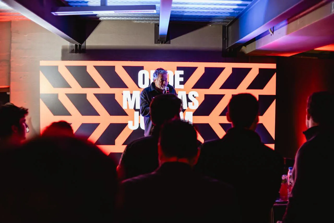 A speaker on stage in front of the LED panel, a field of orange chevrons behind